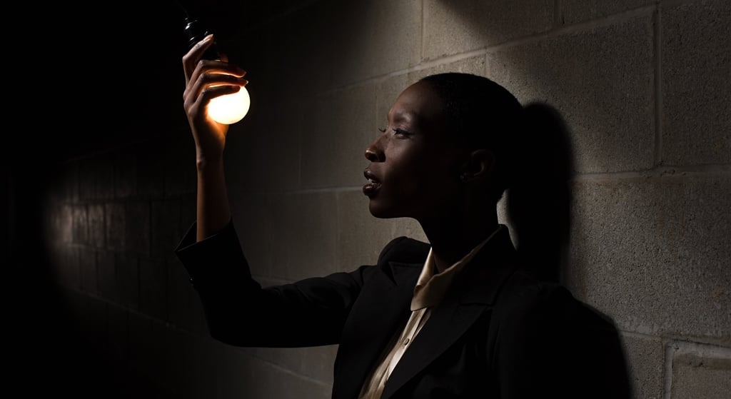 Bald African Business woan holding a lightbulb in a dark room.