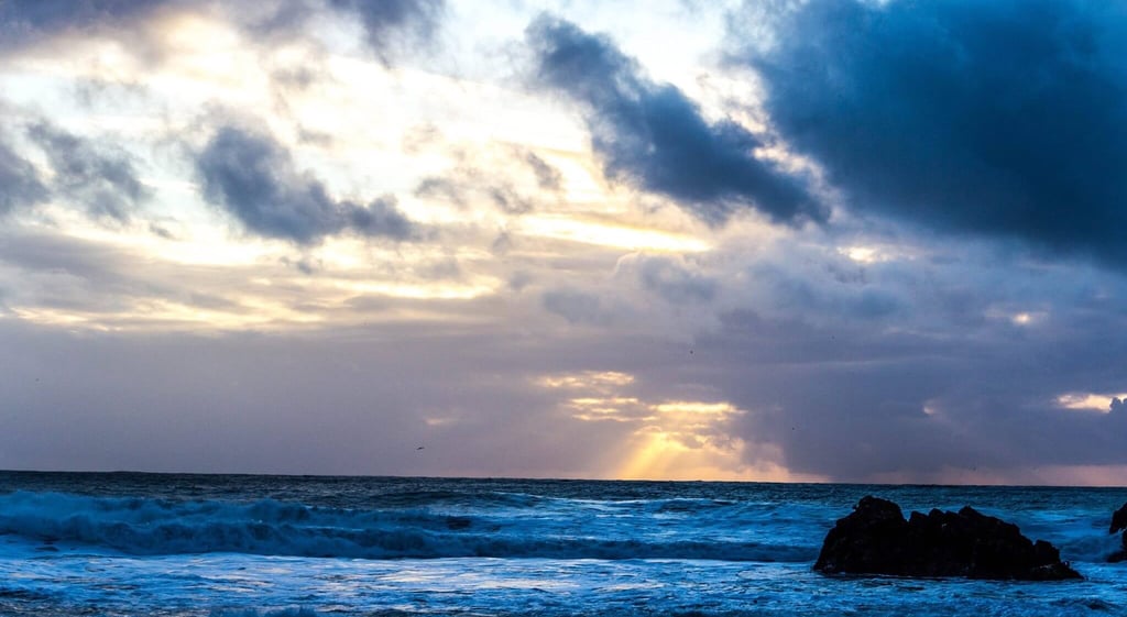 A sunrise breaking through storm clouds over shifting ocean waves