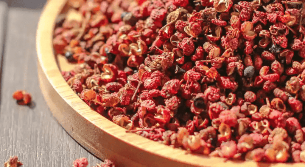 A heap of dried red Sichuan peppers on a round wooden tray, highlighting the spice texture.