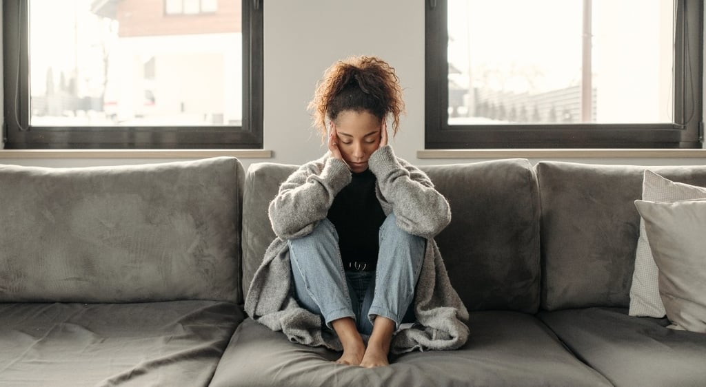 Stressed woman sitting on a couch holding her head, symbolizing mental health and anxiety.