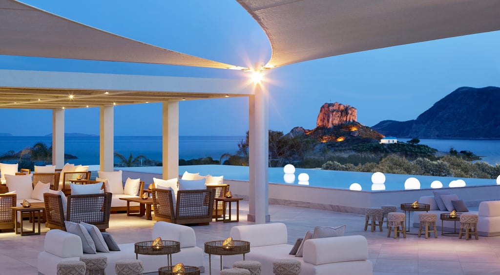 Luxury outdoor resort lounge with white sofas and ocean views at dusk near a cliffside pool.