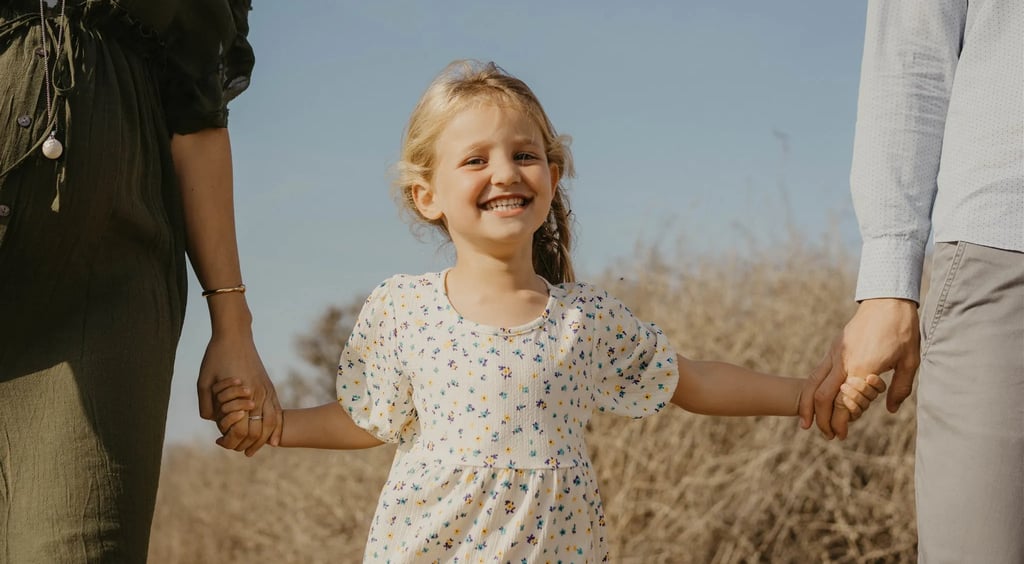 Fillette souriante en pleine nature, tenue par les mains de ses parents – photo de famille naturelle