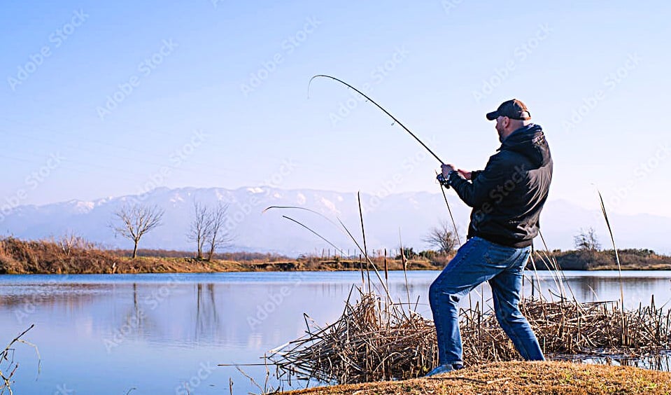 homem pescando tucunaré a beira do lago com vegetação seca ao chao e montanha ao fundo  