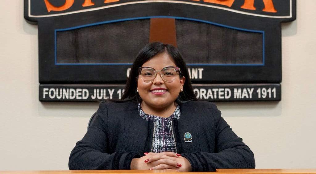 a woman in a black jacket and glasses sitting at a podium