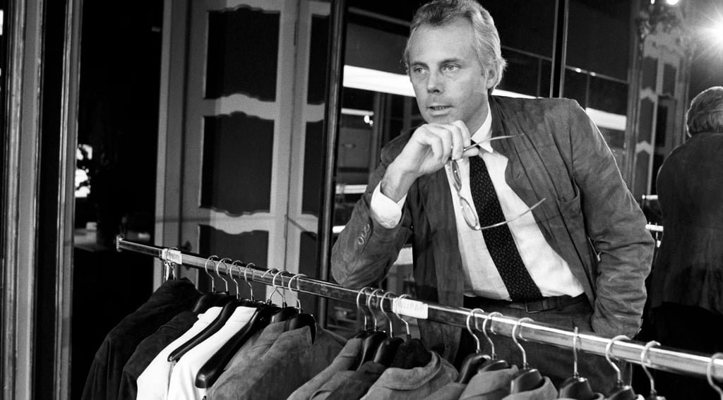 Young Giorgio Armani in his fashion studio with clothing rack.