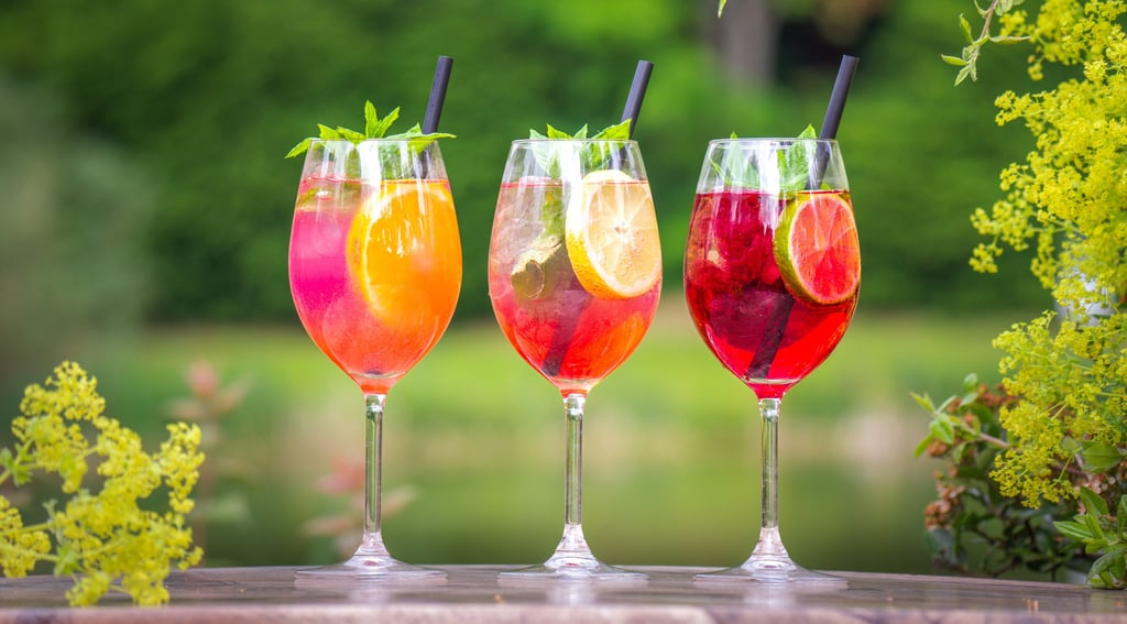 Drei bunte Sommer-Cocktails mit Früchten und Minze auf einer Terrasse.
