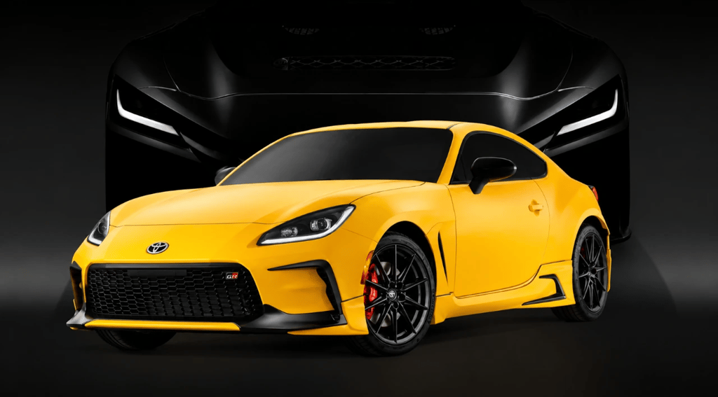 Toyota GR GT amarelo com visual esportivo agressivo e superesportivo V8 ao fundo em cenário escuro.