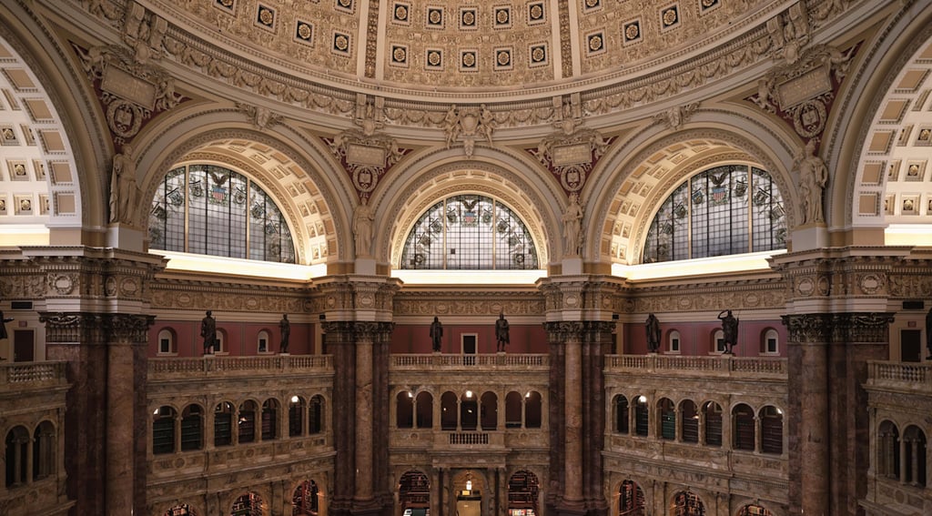 Interior view of a grand, circular library with a domed ceiling and rows of illuminated desks 