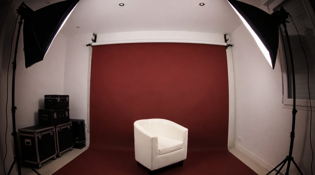 Studio photo avec fond couleu bordeaux fauteuil blanc au centre et deux softbox d’éclairage