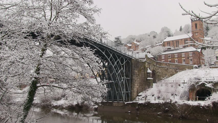 The Iron Bridge in Shropshire covered in winter snow with the Tontine Hotel and church in the background.