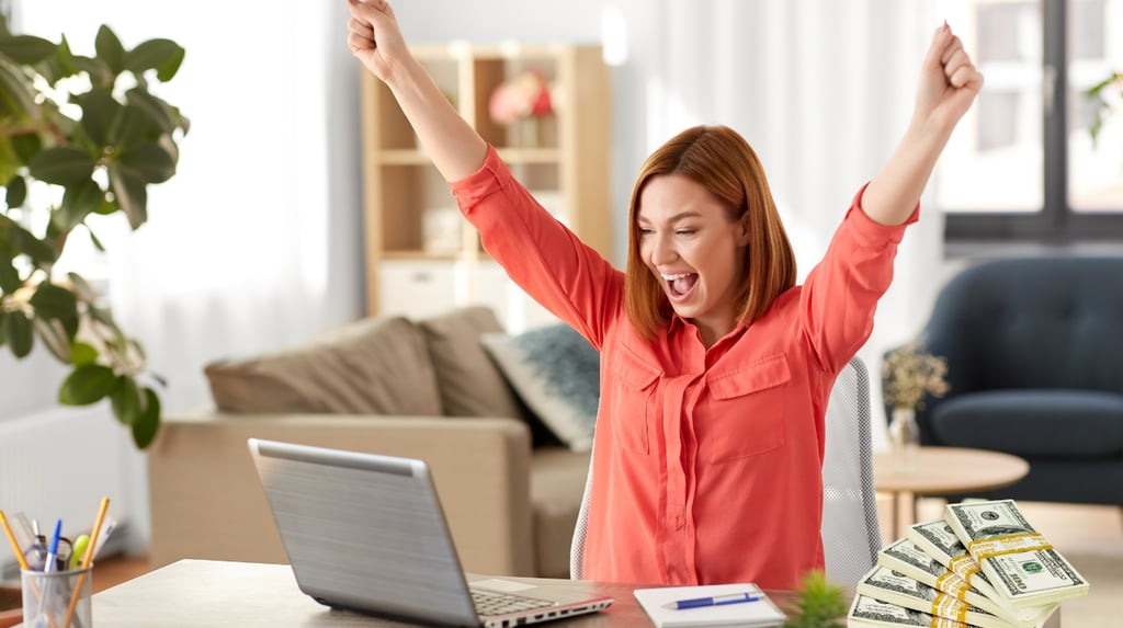 a woman with happy while looking to her laptop with lot of money on the table for boosting sales