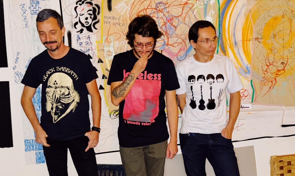 Indie rock band members in graphic t-shirts posing against a graffiti art wall in a music studio.