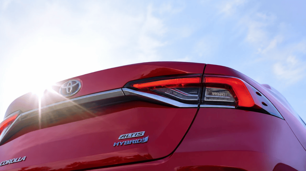 Traseira do Toyota Corolla Hybrid vermelho com iluminação solar e céu azul ao fundo em ângulo baixo.