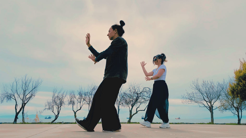 Ebru Tütek and student practicing Bagua walking by the sea, with bare trees and ships in the distance.
