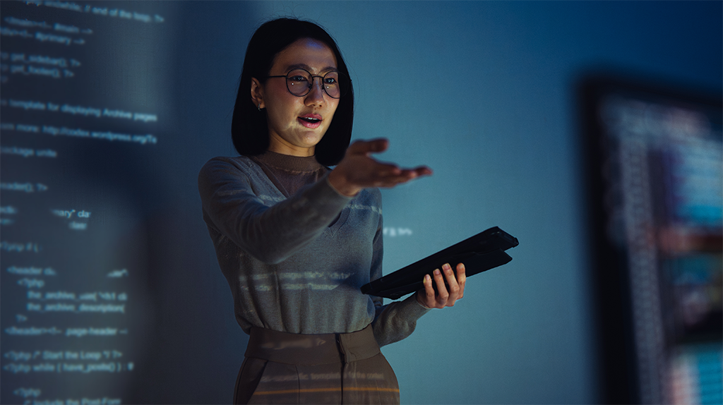 Instructor presenting on a tablet with code projected on a screen in the background