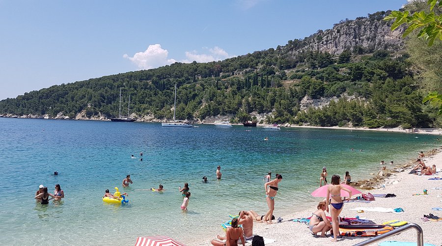 People swimming and relaxing at Kašjuni Beach in Split with crystal clear sea and pine-covered hills in the background