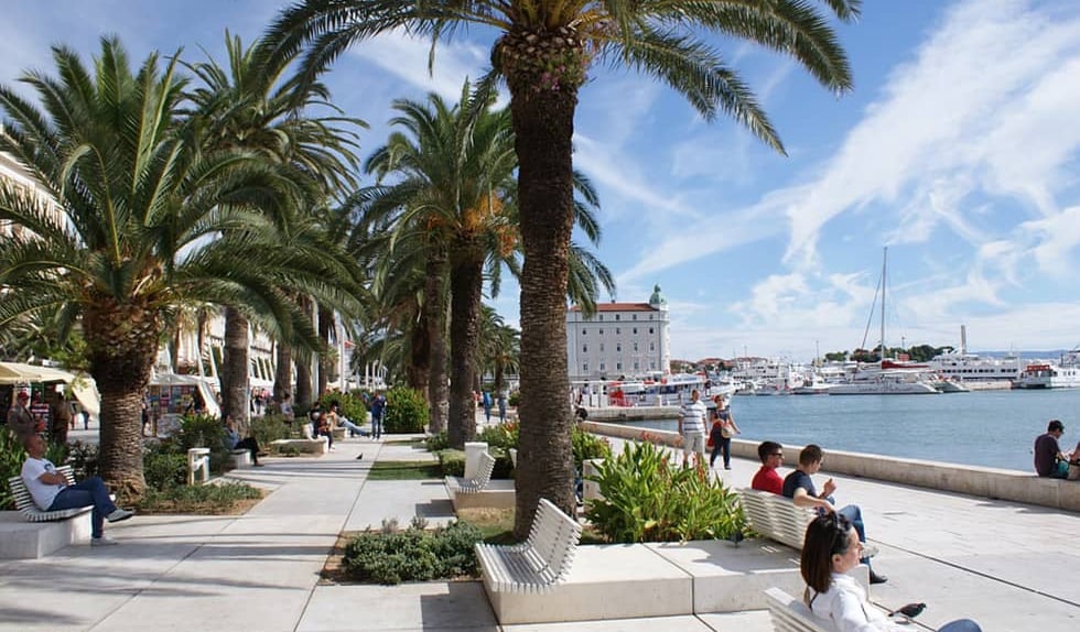 Palm-lined Riva promenade in Split with people walking and boats in the harbour