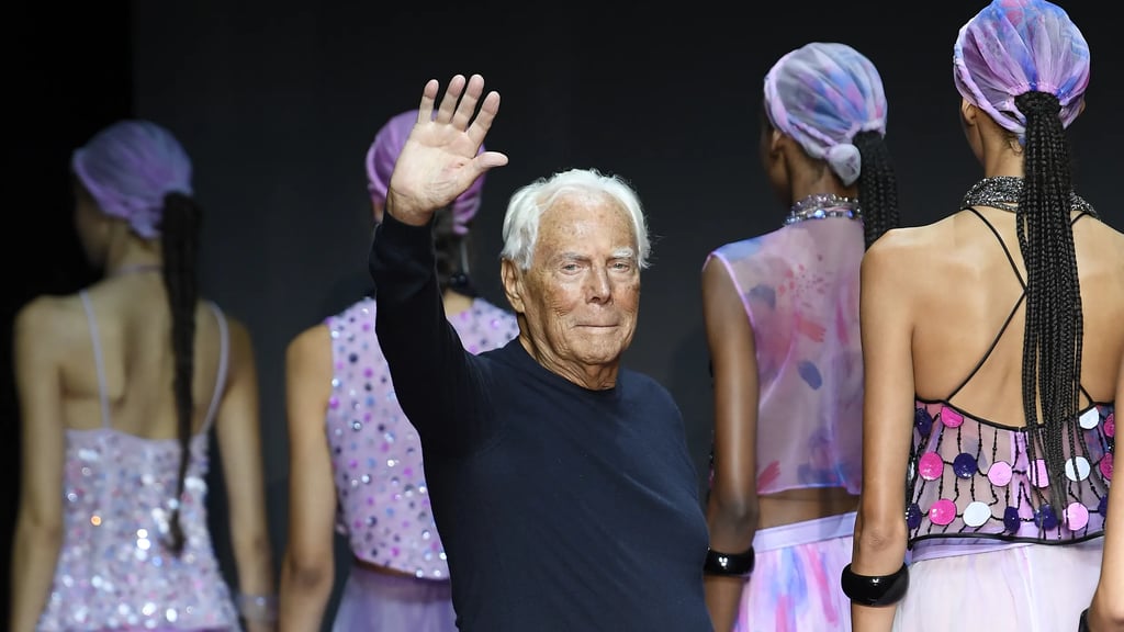Giorgio Armani waves on the runway alongside models in colourful outfits.