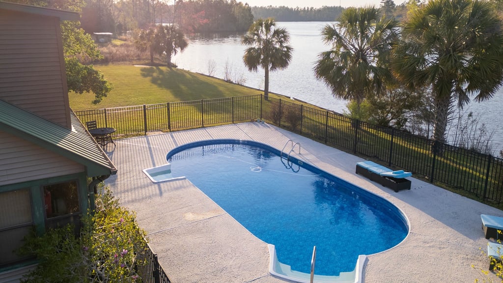 a pool with a fenced in area with a bench and chairs