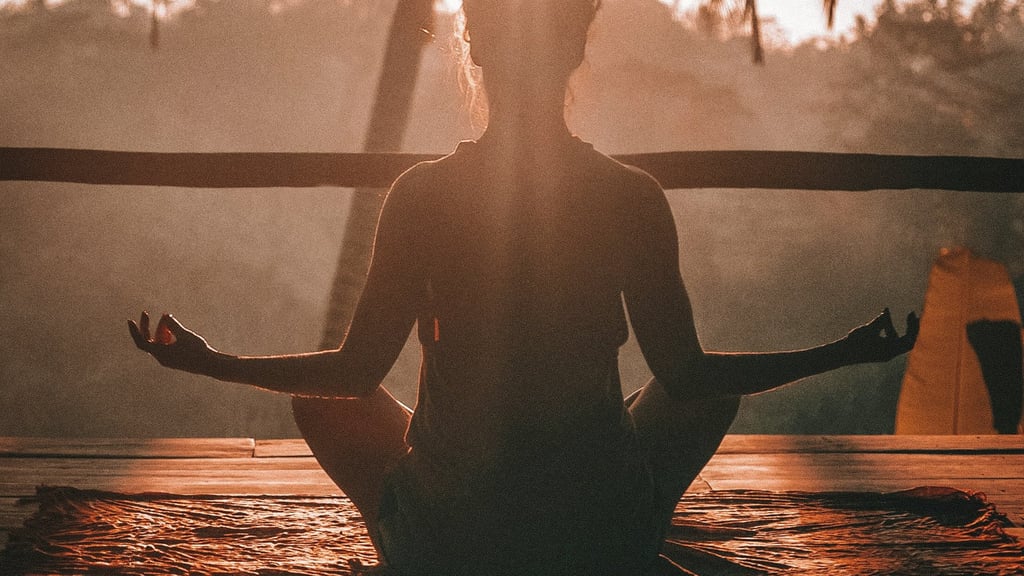 Woman meditating at sunrise in tropical setting, practicing mindfulness, calm, and inner peace.