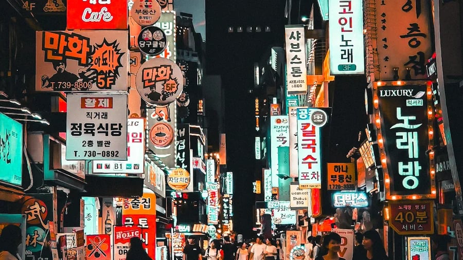 Vibrant night scene of a crowded Seoul street filled with glowing neon Korean business signs and pedestrians.