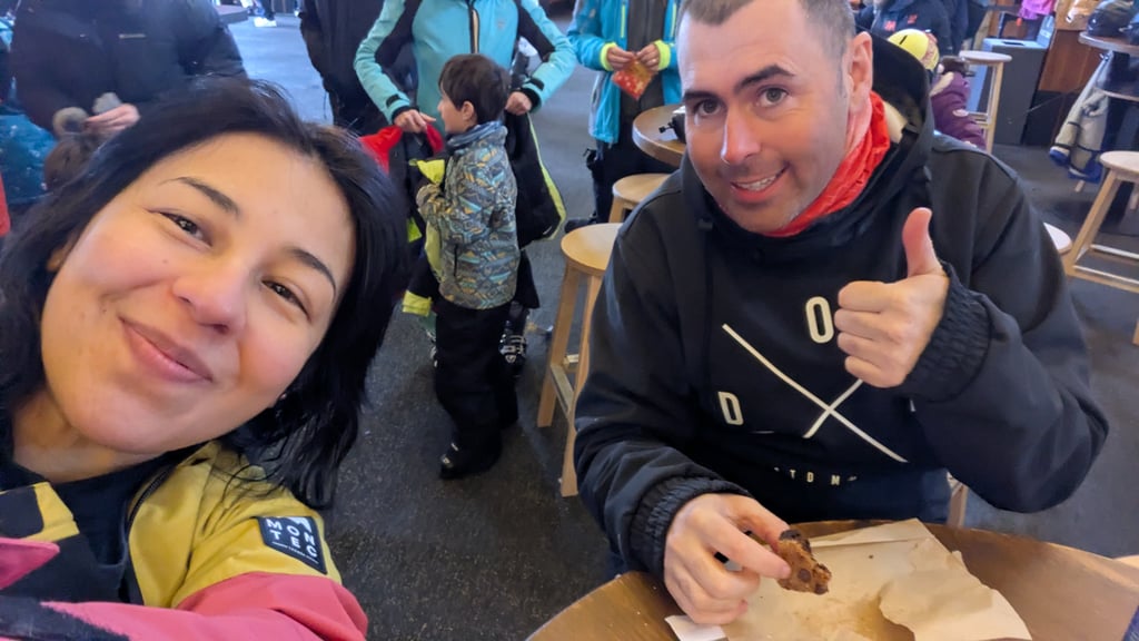 Two people sitting at a table indoors, one giving a thumbs up and holding a cookie.