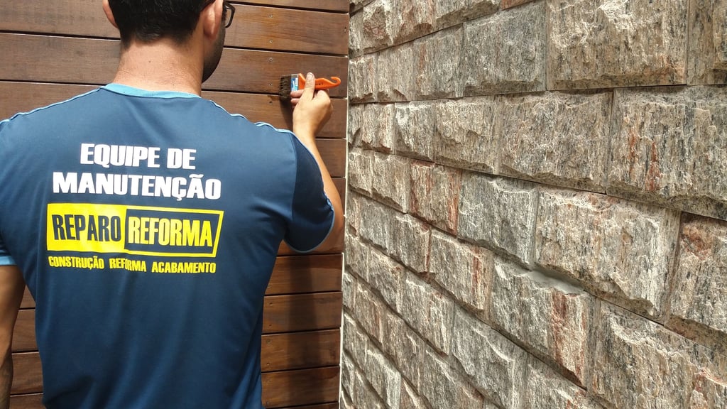 Pintor com um pincel na mao pintando uma parede de madeira ao lado de uma parede de pedras