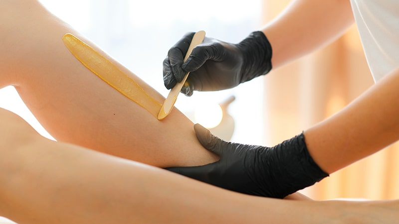 Aplicación de cera depilatoria caliente en la pierna con espátula de madera.