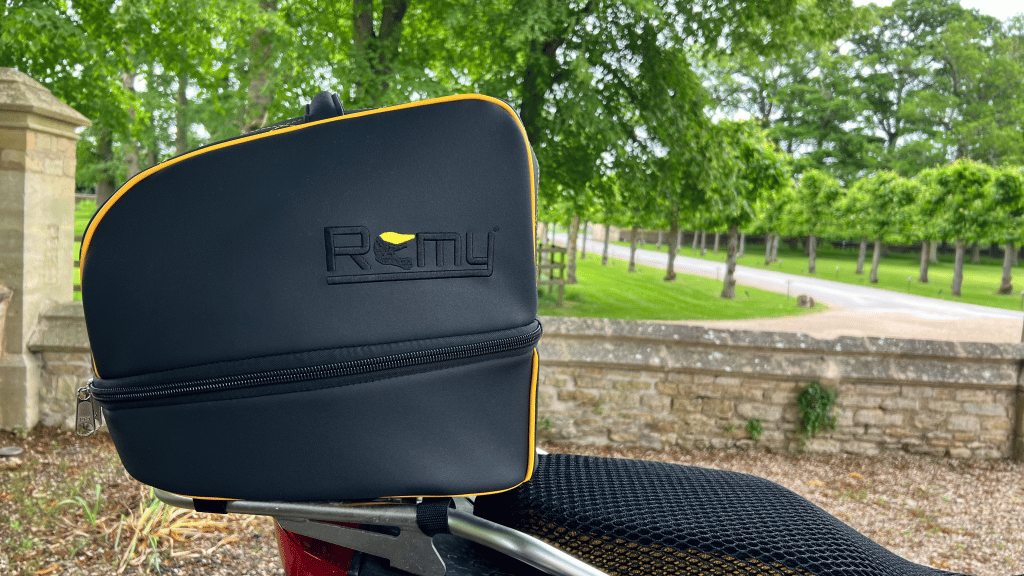 Rider departing on motorcycle with Remy helmet bag secured to the bike, framed against a glowing sun