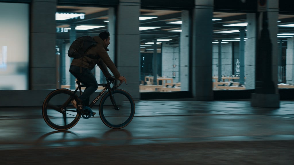 A man on a bicycle rides past a brightly lit shop window at night.