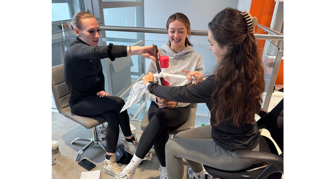 3 people sit together practicing arm bandaging with training materials during a first aid class.