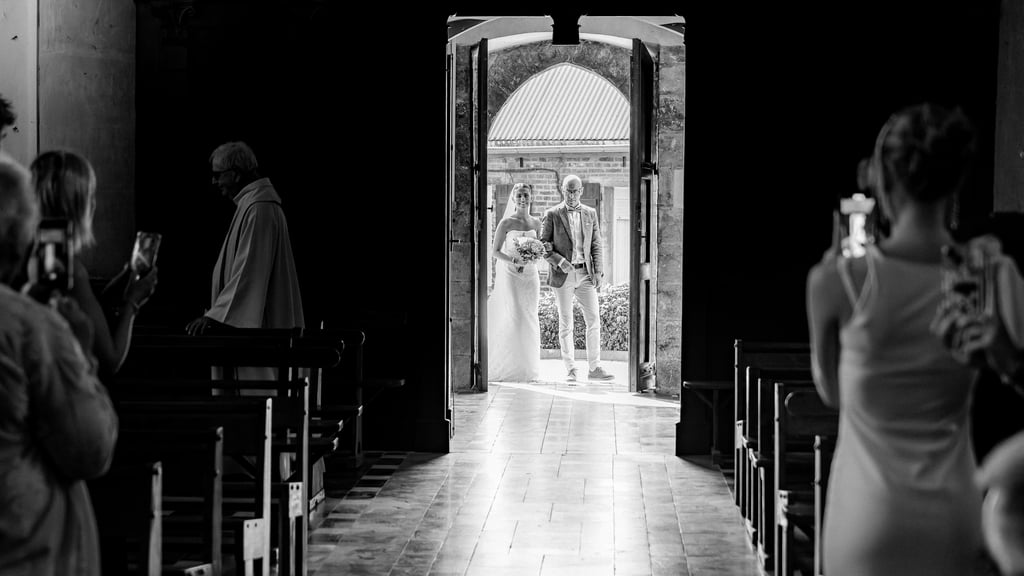 Photo de mariage en noir et blanc d'une mariée et d'un marié entrant dans une chapelle d'église par 