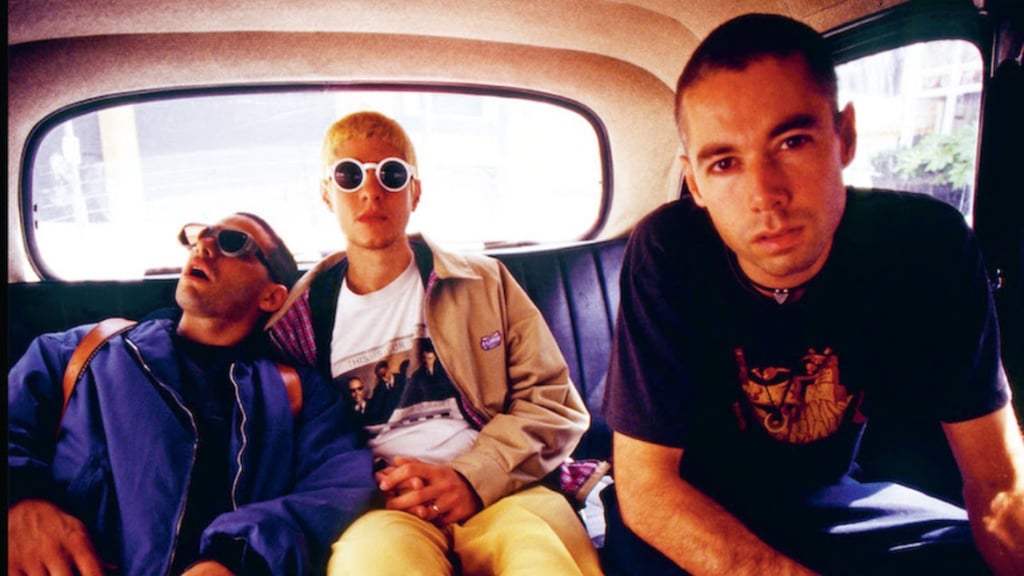 Os três integrantes dos Beastie Boys sentados no banco traseiro de um carro.