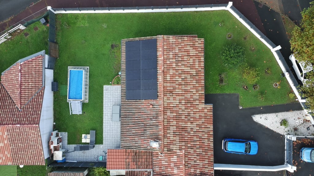 Vue aérienne d'une maison avec panneaux solaires sur le toit et une piscine à l'arrière de la maison