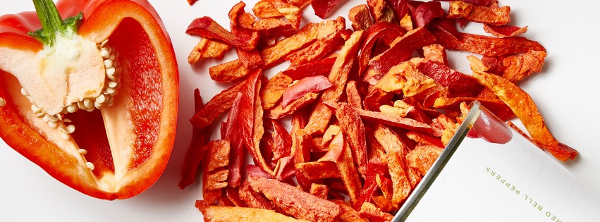 A whole red pepper next to a sliced piece of Thrive freeze-dried red pepper