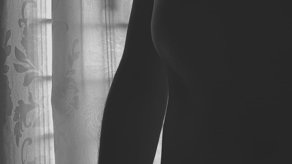 Silueta artística de cuerpo masculino en blanco y negro ante cortina.