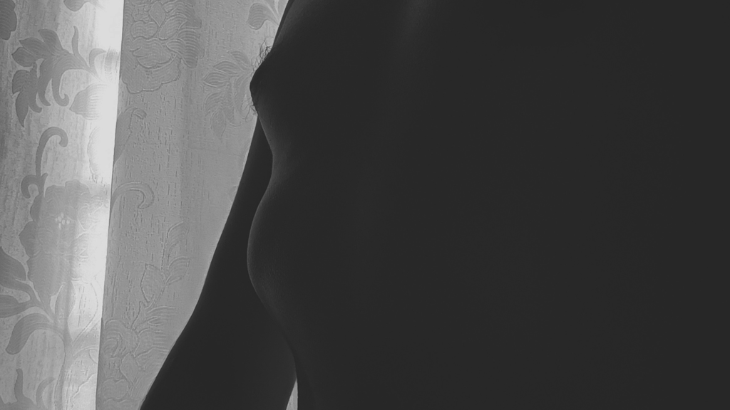 Silueta de pecho y torso masculino en blanco y negro ante cortina.