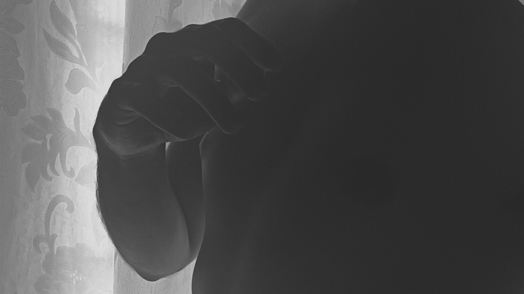 Primer plano de mano y torso en sombras frente a luz de ventana.