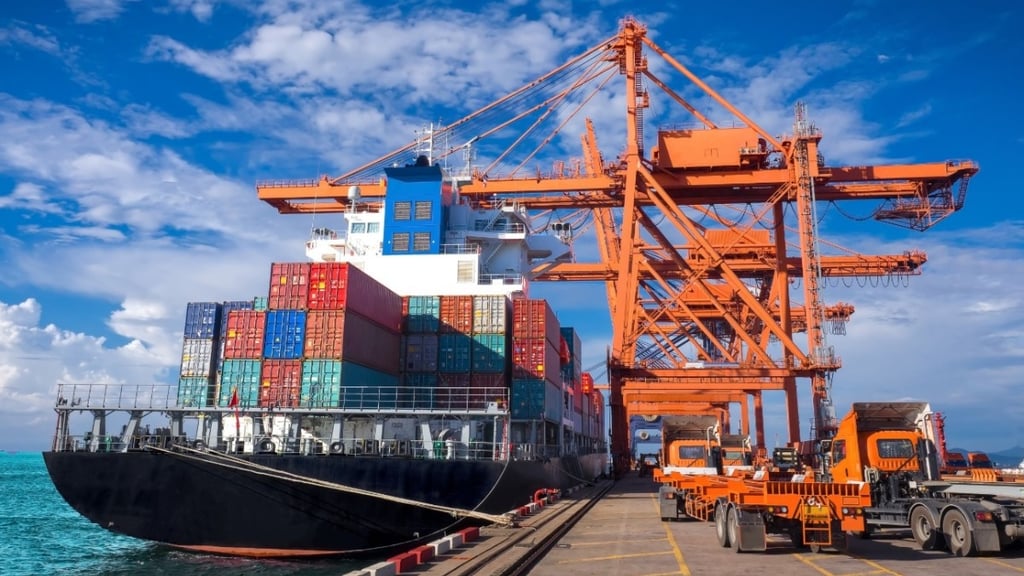 Um navio cargueiro gigante ancorado em um porto com guindastes e caminhões.