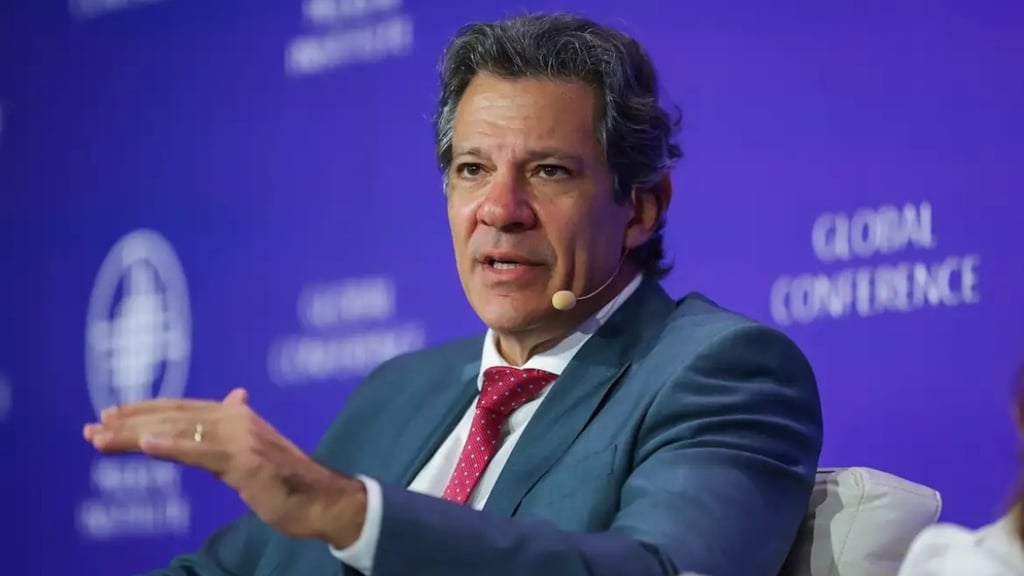  Fernando Haddad, de terno e gravata vermelha, em uma conferência, gesticulando com a mão.