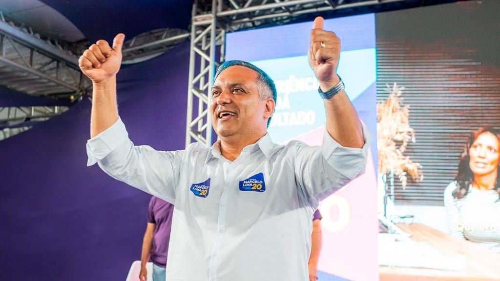 Marcelo Lima com uma camisa social branca, erguendo os polegares em um evento político.