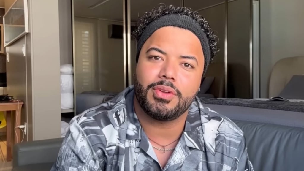 Hytalo em close, com um gorro preto, camisa estampada e barba.