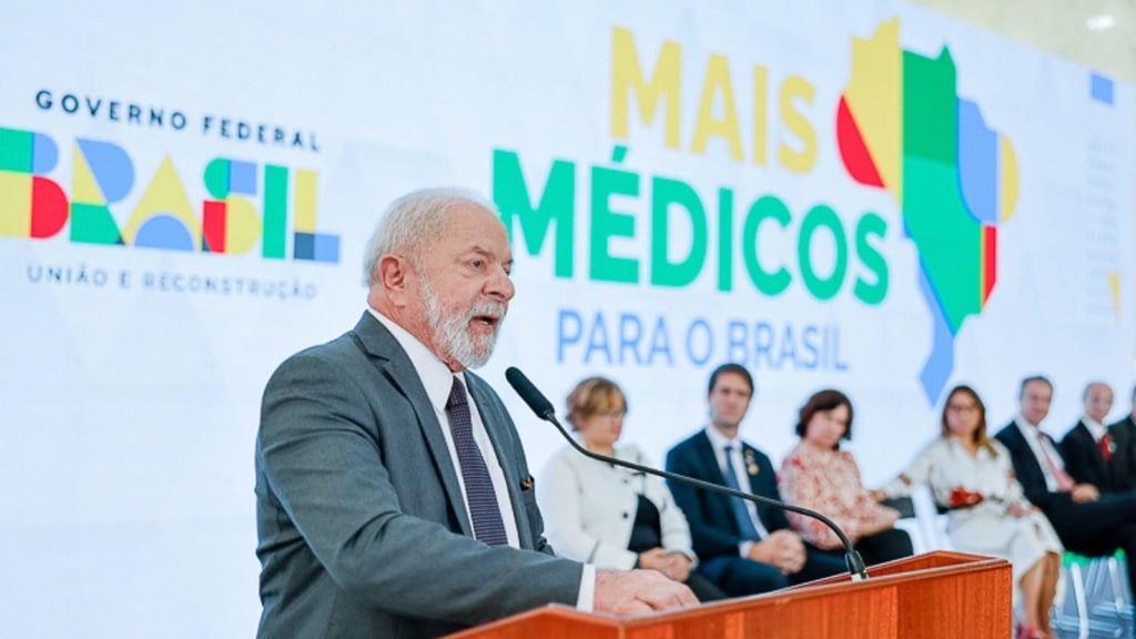 Lula discursando no pódio em um evento do programa "Mais Médicos" do Governo Federal.