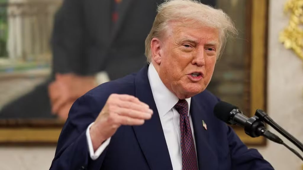 Donald Trump gesticula durante um discurso, com terno azul e gravata vermelha, em um ambiente forma