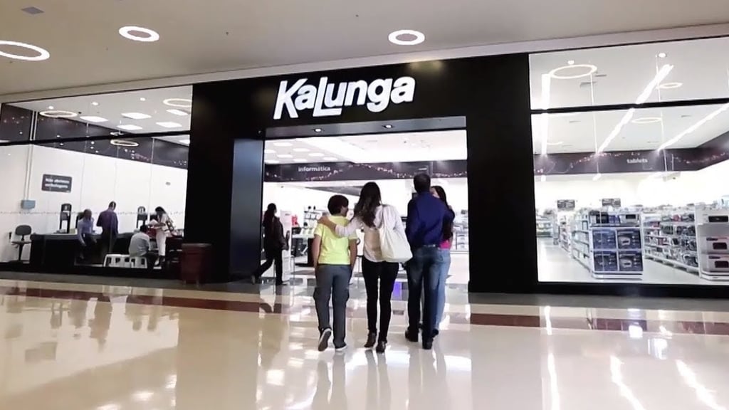  Família entra em uma loja da Kalunga em um shopping center, com outros clientes ao fundo.