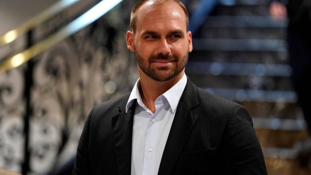  Eduardo Bolsonaro de terno, com barba, olhando para o lado e sorrindo levemente.