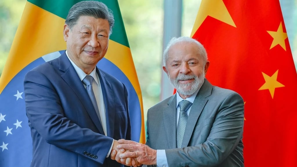 Xi Jinping e Lula apertam as mãos na frente das bandeiras do Brasil e China.