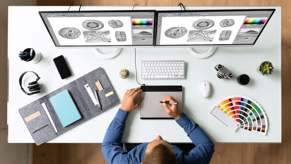 a man sitting at a desk with a laptop and a computer sketching graphics