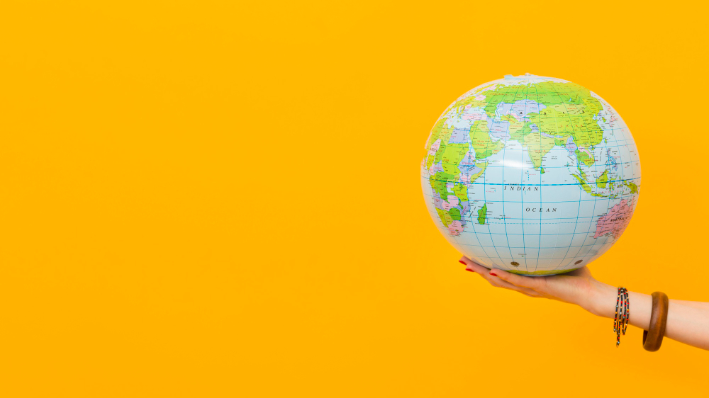A person holding an inflatable world globe against a vibrant yellow background for global travel concepts.