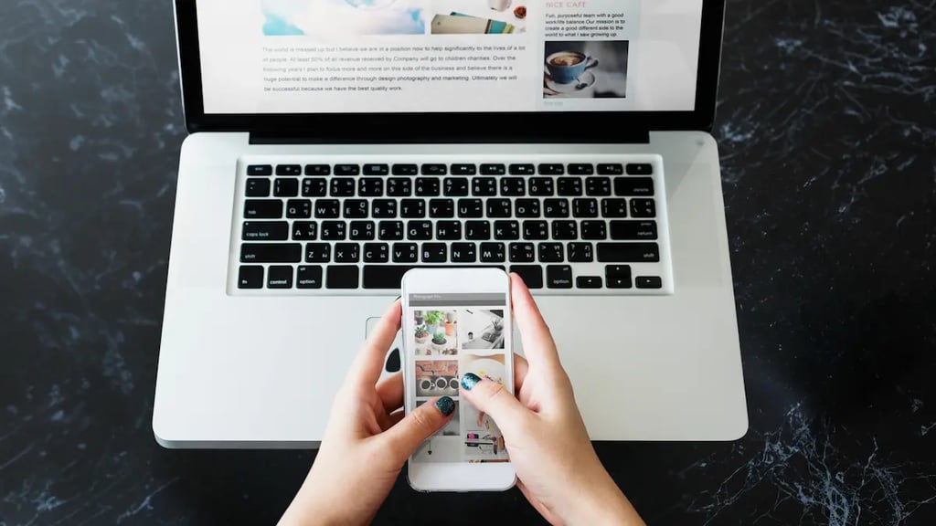 Manos utilizando un smartphone para navegar en un sitio optimizado para móviles frente a un portátil